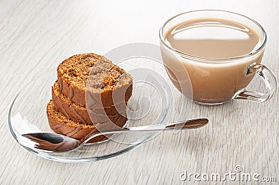 Stack of slices of swiss roll, spoon in saucer, cup of cocoa with milk on wooden table Stock Photo
