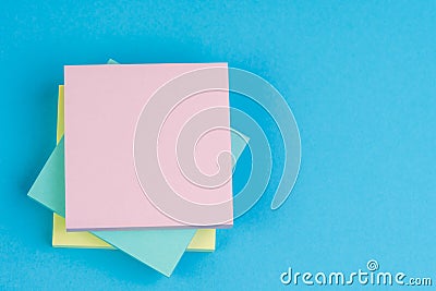 Stack of sticky notes on solid blue background with yellow, blue and pink on top with copy space for writing message using as memo Stock Photo