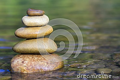 Stack of stones balancing on top in green water of the river Stock Photo