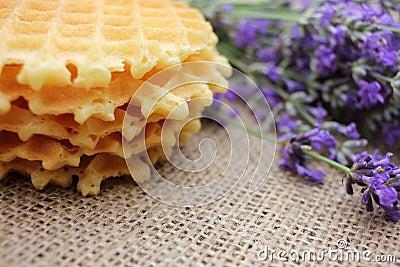 Stack of waffles and bunch of lavender on a burlap fabric texture background. Stock Photo