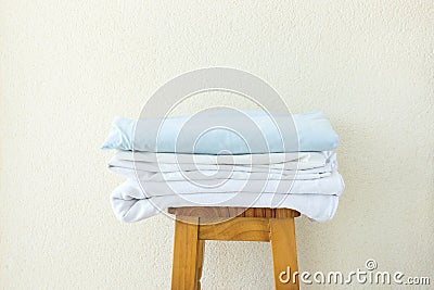 Stacked clean folded cotton bedlinen on wooden stool white wall background. Laundry washing cleanliness concept Stock Photo