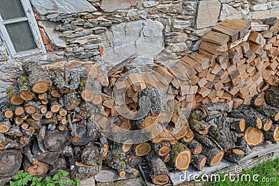 Stacked firewood wood lumber timber stack logs and trunks pile by a historic cottage cottage Stock Photo