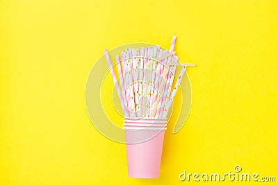 Stacked Pink Drinking Paper Cups with Striped Straws on Yellow Background. Flat Lay Composition. Birthday Party Celebration Kids Stock Photo