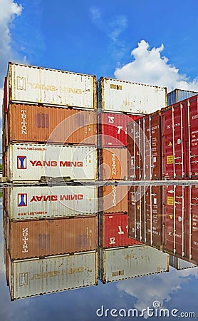 Stacked shipping containers reflect in puddle, blue sky and clouds Editorial Stock Photo