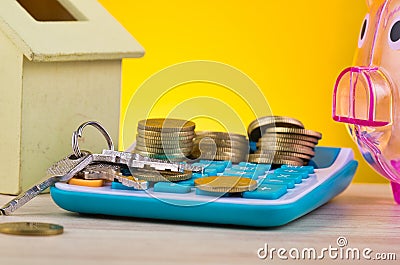 Stacking coins and bunch of key on calculator, piggy bank and house replica on wooden desk Stock Photo