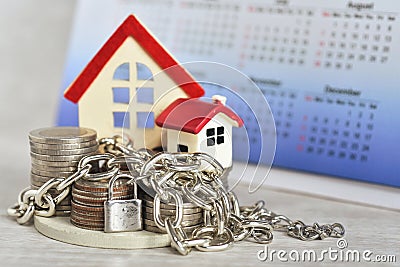 Stacking coins for house loan monthly installment with the metal cahin and lock pad infront of the red roof house and the desk cal Stock Photo