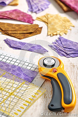 Stacks of multi-colored pieces of fabric, cutting mat, ruler, rotary cutter on a white surface Stock Photo