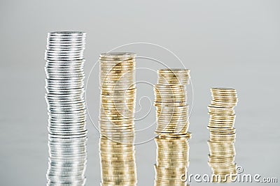 Stacks of silver and golden coins on surface with reflection isolated on grey. Stock Photo