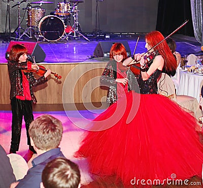 On stage, the expressive red-haired violinist Maria Bessonova sons twins. violin trio two generations of red fiery musicians. Editorial Stock Photo
