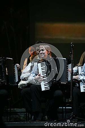 On stage, the musicians and soloists of Orchestra of accordionists (harmonic orchestra) under the baton of conductor. Editorial Stock Photo