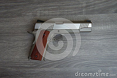 Stainless hand gun with brown hand grip is on the wooden floor Stock Photo