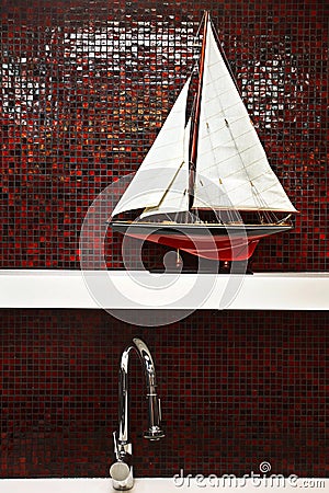 Stainless steel faucet with sailboat model on shelf with red pat Stock Photo