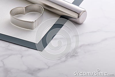 Stainless steel heart-shaped cookie cutter and rolling pin lying on baking mat Stock Photo