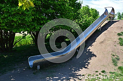 Stainless steel slide on a playground with grassy hills. playground with stone walkways made of natural sandstone stone. a pipelin Stock Photo