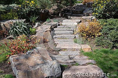 Staircase made of massive stones among blooming flowers in the park Stock Photo