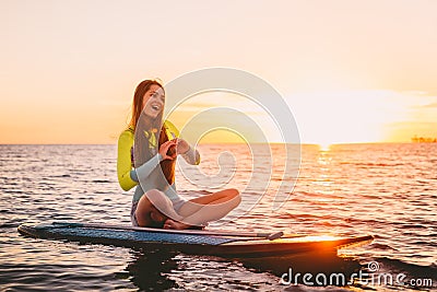 Stand up paddle boarding on a quiet sea with warm summer sunset colors. Happy smiling girl on board at sunset Stock Photo