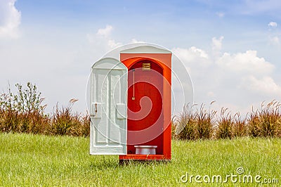 Standalone of red toilet with white door open contrast with green grass and tree in the meadow. Stock Photo