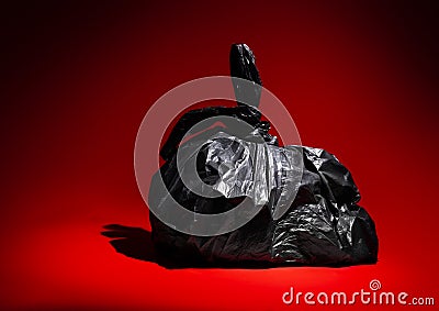 Black plastic trash bin bag spotlit on a red background Stock Photo