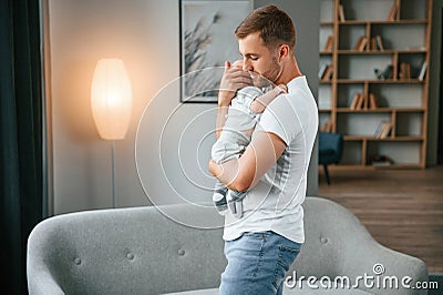 Standing with baby in hands. Father with toddler is at home, taking care of his son Stock Photo