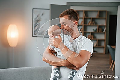 Standing with baby in hands. Father with toddler is at home, taking care of his son Stock Photo