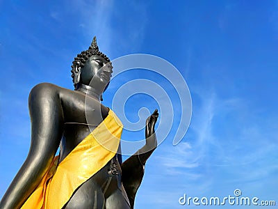 Standing Black Buddha statue Sukhothai style Wear yellow cloth and sky Stock Photo