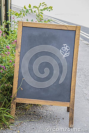 Standing chalkboard sandwich sign sitting outside on rough pavement with a rough flower drawn in corner - room for copy and some Stock Photo