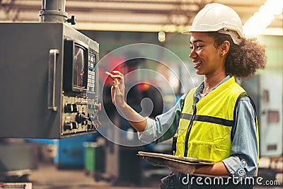 Standing in front of a control panel, a female industrial electrical engineer with a safety hardhat on her head and a tablet in Stock Photo