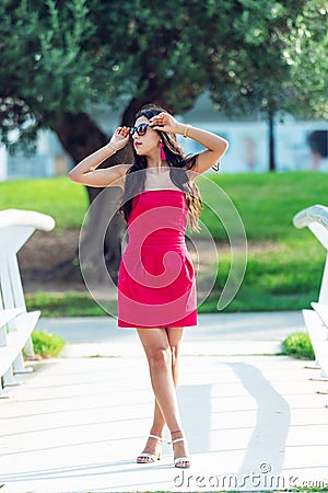 Standing girl young Latina, long-haired brunette in red dress with crossed legs Stock Photo
