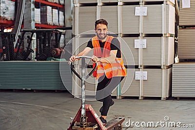 Standing with platform trolley. Storage worker is in the warehouse with bunch of products Stock Photo