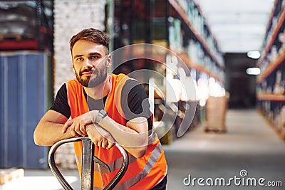 Standing with platform trolley. Storage worker is in the warehouse with bunch of products Stock Photo