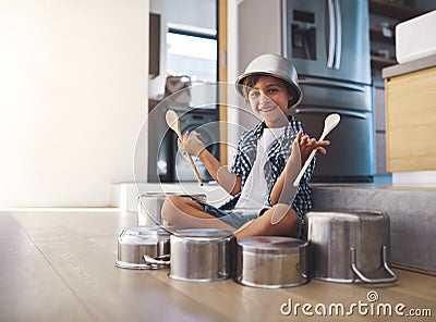 Stardom, here I come. Portrait of a happy little boy playing drums with pots on the kitchen floor while wearing a bowl Stock Photo