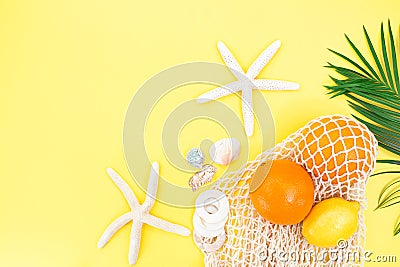 Starfish, shells with bag string bag with oranges and lemon with palm branch from the side on yellow background. Concept of summer Stock Photo