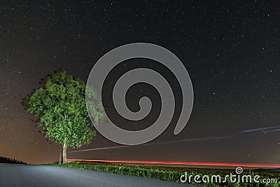 Starry sky in summer with a tree lit up with traces of light on a street, Germany Stock Photo