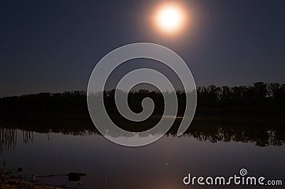 the stars in the night sky are reflected in the mirror smooth surface of the lake, and the moon illuminates Stock Photo