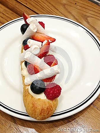 Start your day with homemade Gourmet pastry Choux Cream or eclair top with raspberry, blueberry and tiny meringue on white dish, f Stock Photo