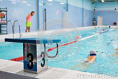 Starting platform with number three is in four lanes swimming pool for children groups. Kids do exercises with an instructor Stock Photo