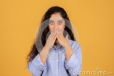 Startled young woman with voluminous curly hair covering her mouth with hands Stock Photo