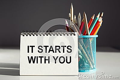 IT STARTS WITH YOU - inscription on a notebook with colored pencils Stock Photo