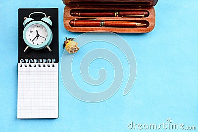 Stationery layout on a blue background - a notebook on a spring, parkers and a vintage alarm clock. Stock Photo