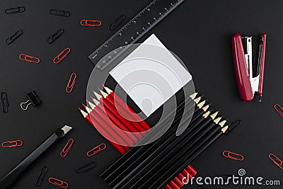 Pencils in black and red, stapler, red and black clips, ruler and knife, white paper on a black background Stock Photo