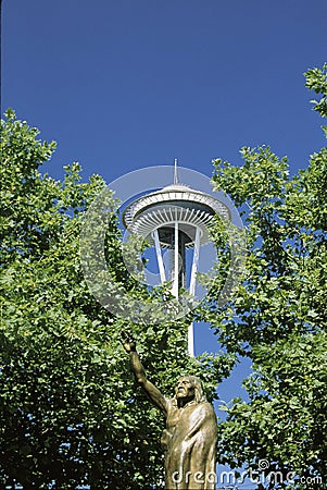 This is a statue of Chief Seattle in front of the Space Needle. There is green summer foliage on the trees surrounding the Editorial Stock Photo