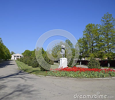 Statue of a collective farmer on a pedestal. The legacy of the Soviet era. A flower bed with tulips and young trees in Stock Photo