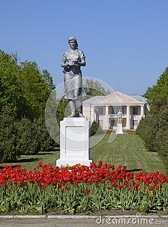 Statue of a collective farmer on a pedestal. The legacy of the Soviet era. A flower bed with tulips and young trees in Stock Photo