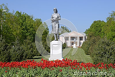 Statue of a collective farmer on a pedestal. The legacy of the Soviet era. A flower bed with tulips and young trees in Stock Photo