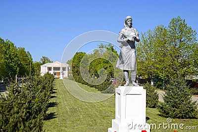 Statue of a collective farmer on a pedestal. The legacy of the Soviet era. A flower bed with tulips and young trees in Stock Photo