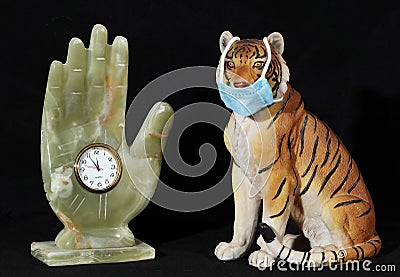 Statuette of a Tiger in a medical mask and a hand with a clock Stock Photo