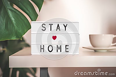 Stay home concept. Self isolation during Covid-19 coronavirus pandemic. STAY HOME written on light board and cozy home blurry Stock Photo