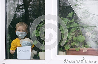 Stay at home quarantine for coronavirus pandemic prevention. Sad child and his teddy bear both in protective medical masks sits on Stock Photo