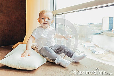 Stay Home Stay Safe. Little cute sweet infant little baby girl sitting near large window in bright light living room at home Stock Photo