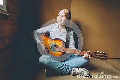 Stay Home Stay Safe. Young woman sitting in room on floor and playing guitar at home. Teen girl learning to play song Stock Photo